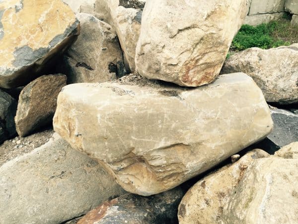 Stacked large boulders in shades of beige, brown, and gray with rough textures, forming a natural or landscaped feature in Long Island, NY.