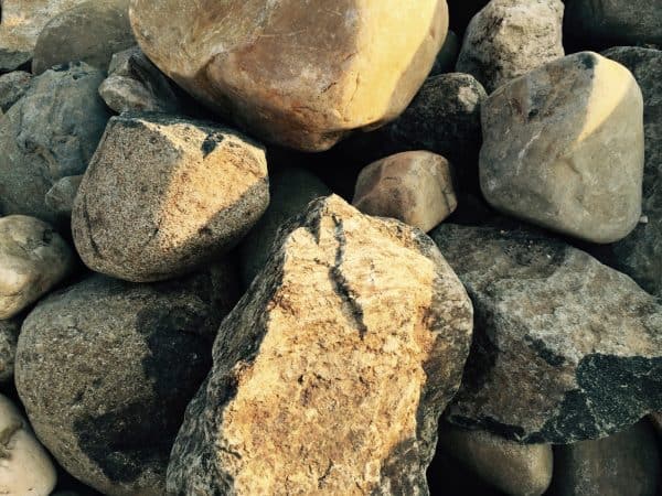 Stacked large boulders in shades of beige, brown, and gray with rough textures, forming a natural or landscaped feature in Long Island, NY.