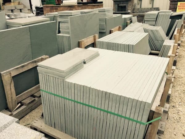 Stacks of large rectangular stone slabs secured with green straps on wooden pallets in an outdoor construction supply yard in Long Island, NY.