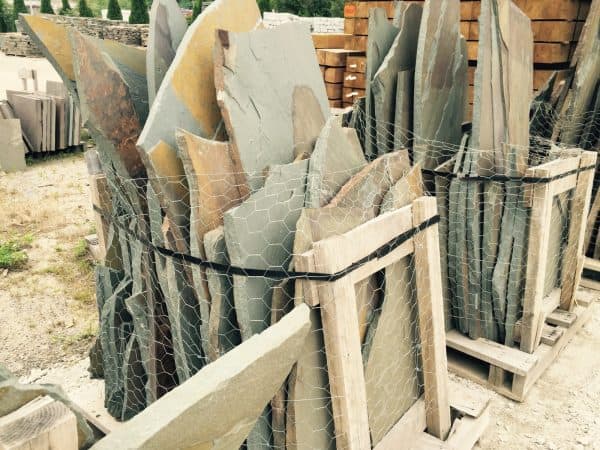 Stacked stone slabs secured in wooden frames with wire mesh and straps, stored outdoors for landscaping or construction use in Long Island, NY.
