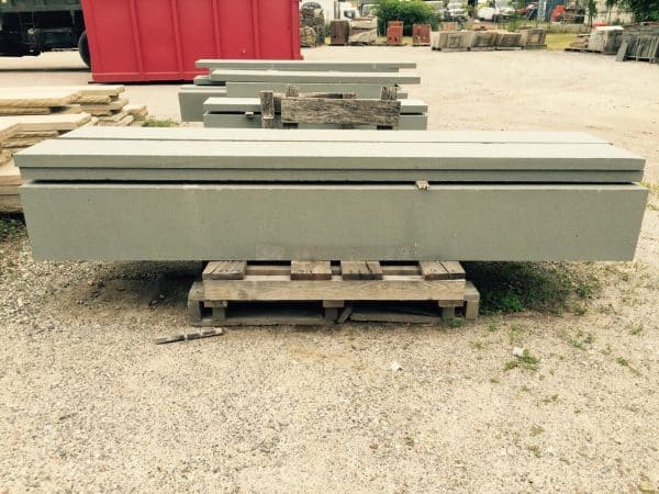 Large concrete beam resting on a wooden pallet at a construction site with stacked beams and equipment in the background in Long Island, NY.