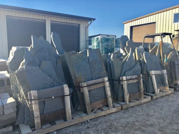 Irregular stone slabs stacked vertically on wooden pallets and secured with frames and wires in a construction supply yard in Long Island, NY.